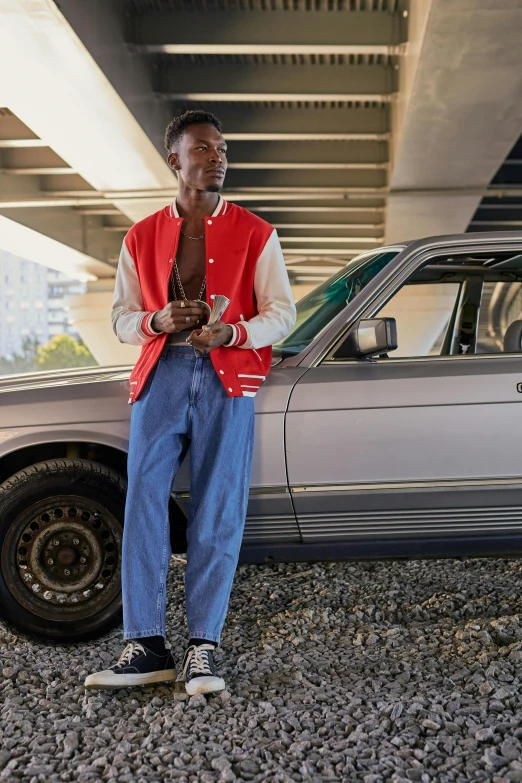 a black man wearing a red vest standing next to a silver car