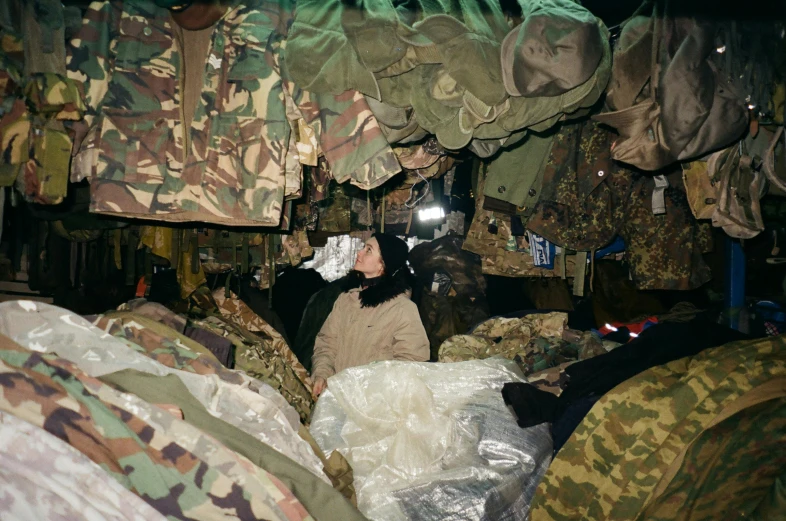 a man standing next to a pile of clothes in a camouflage room