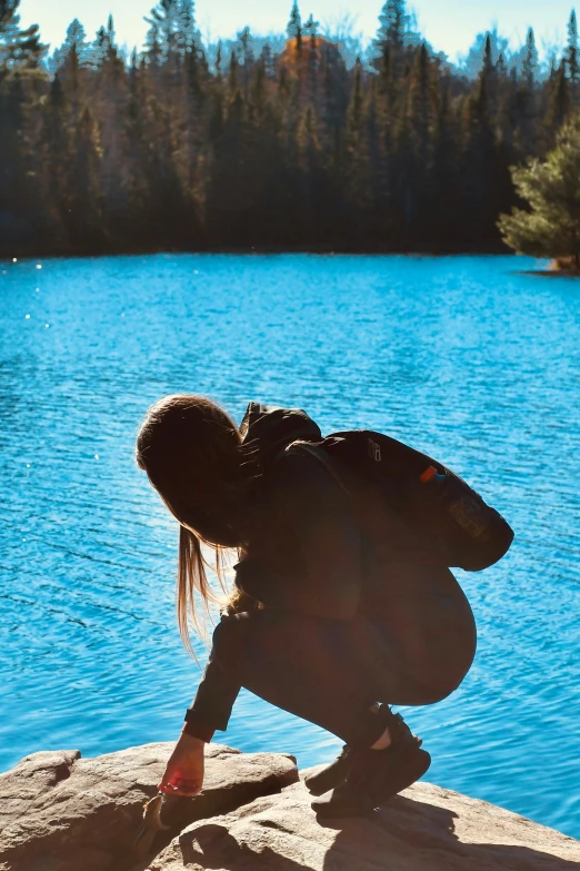 a woman kneeling on a rock beside the water