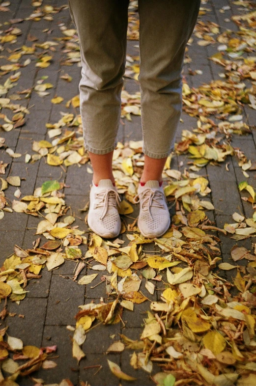 a woman in white sneakers standing on top of leaves