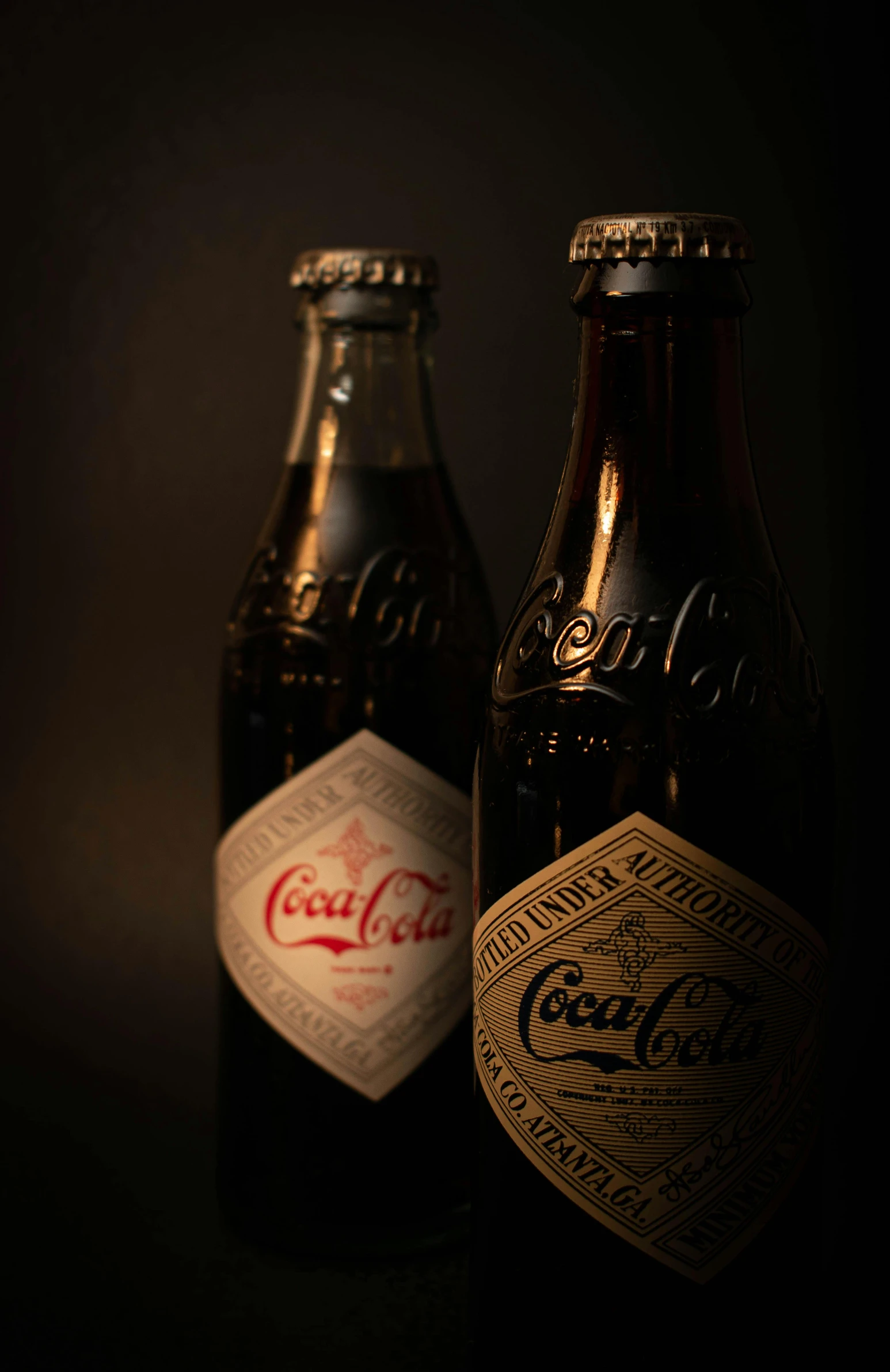two dark brown soda bottles with coca - cola labels