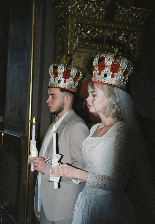 two people wearing crowns are looking at a candle