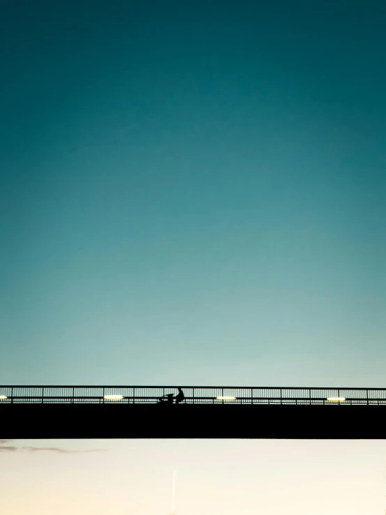 this person on a bridge is silhouetted against the blue sky