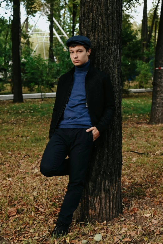 a young man leans against a tree in the middle of the forest