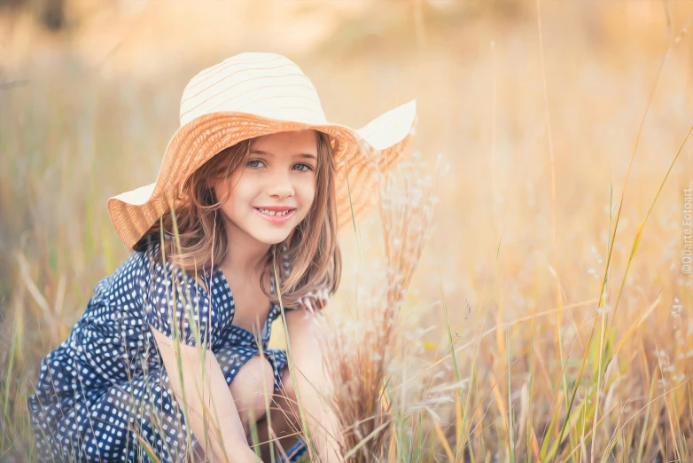 little girl in hat sitting in the tall grass