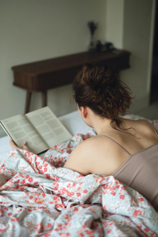 a young woman laying in bed reading a book