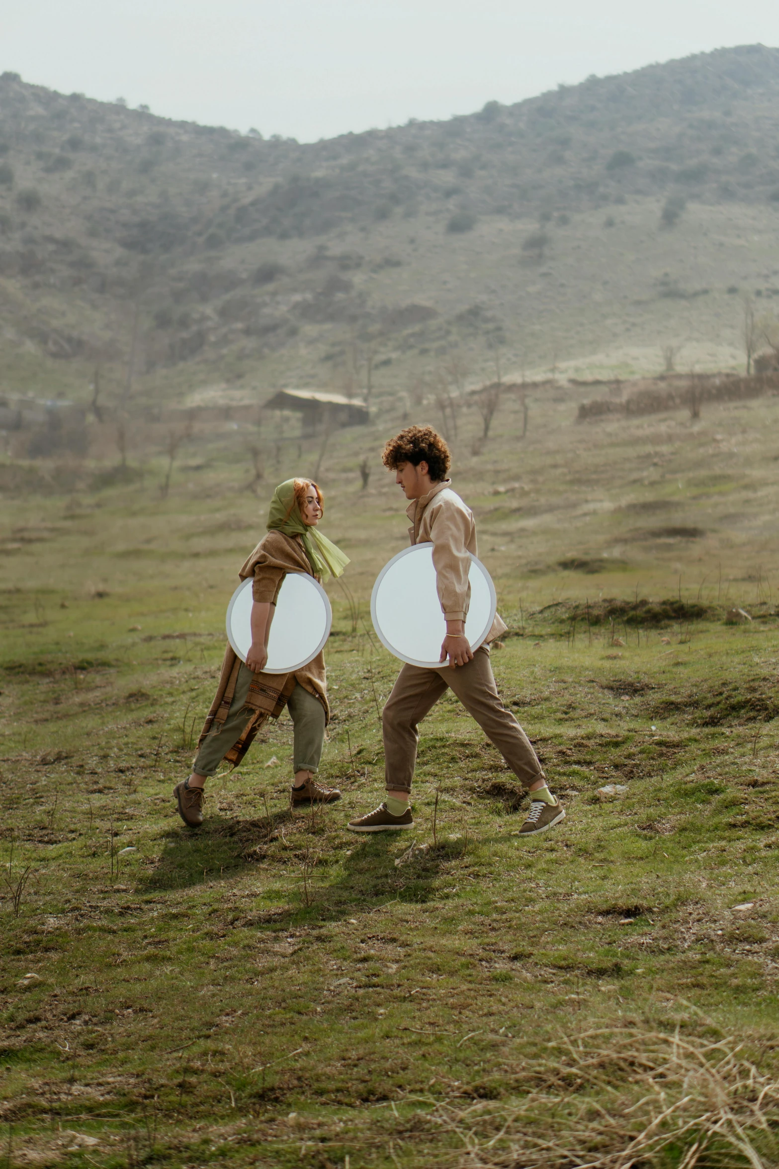 two people are walking on the grass with frisbees in hand