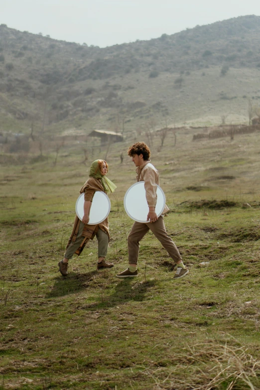 two people are walking on the grass with frisbees in hand