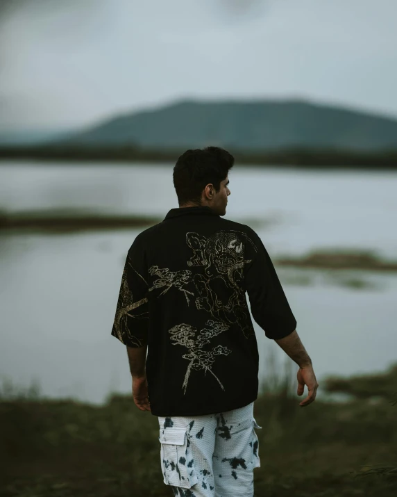 a man wearing floral clothing standing next to a lake