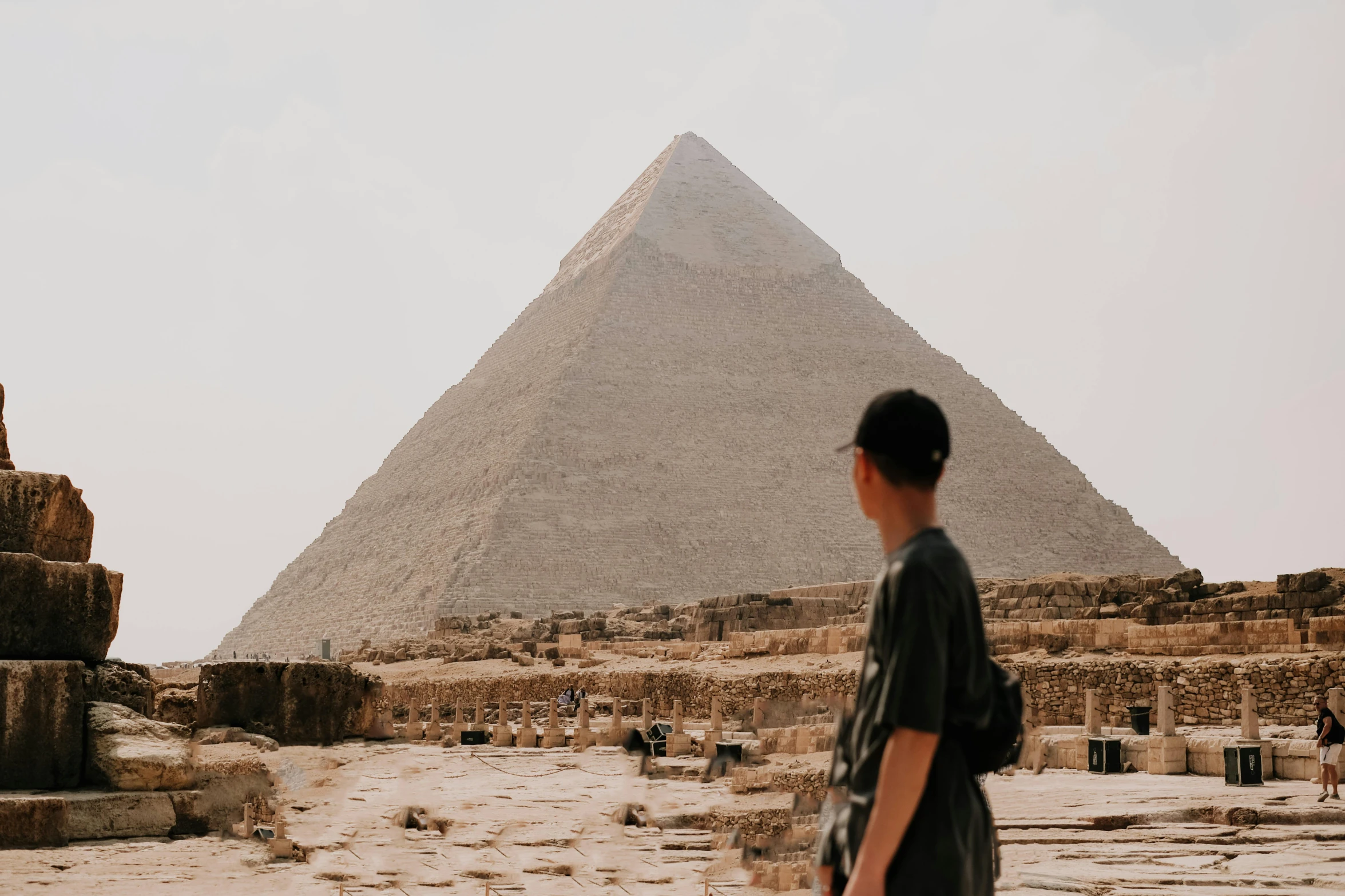 man with dark hair wearing shirt looking up at pyramids