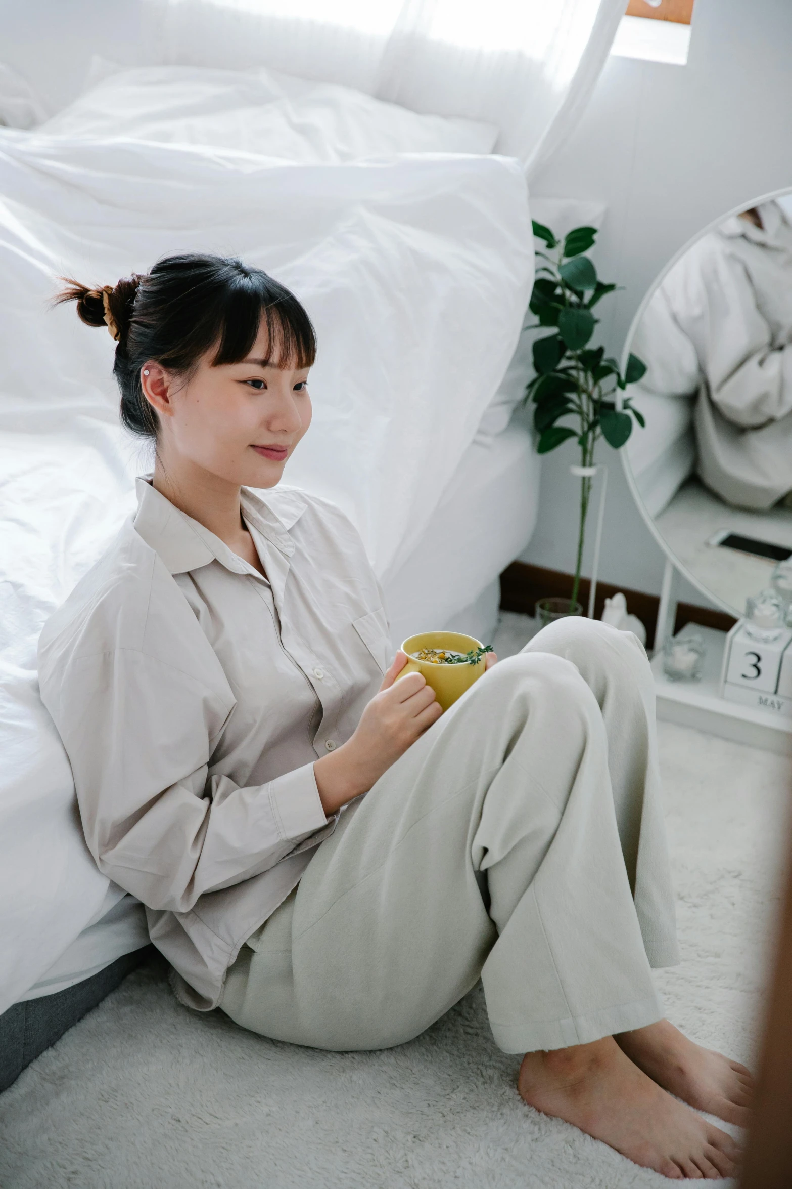 an asian woman sitting on the floor drinking from a mug