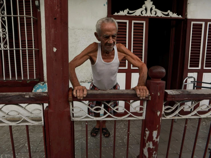 an old man leans on a railing of a red building