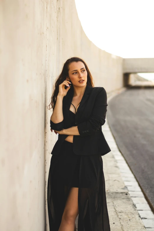 the woman is leaning against the wall wearing a long black dress