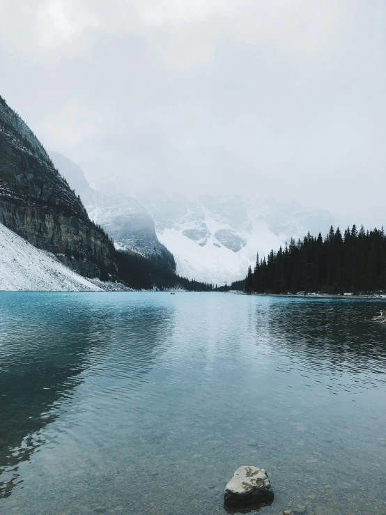 a mountain range reflects the sky and snow on a calm lake