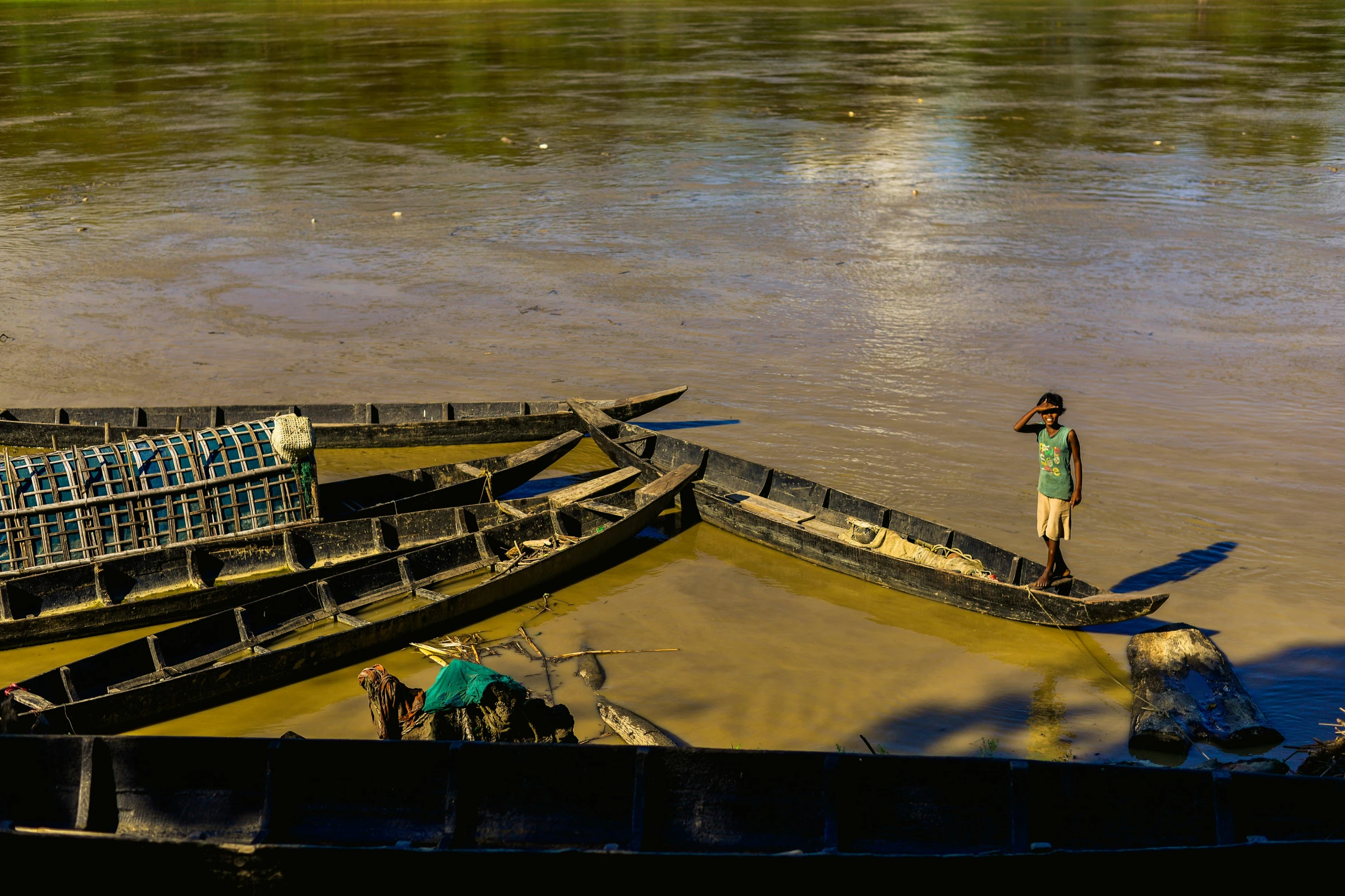 the boy is standing by the wooden boat