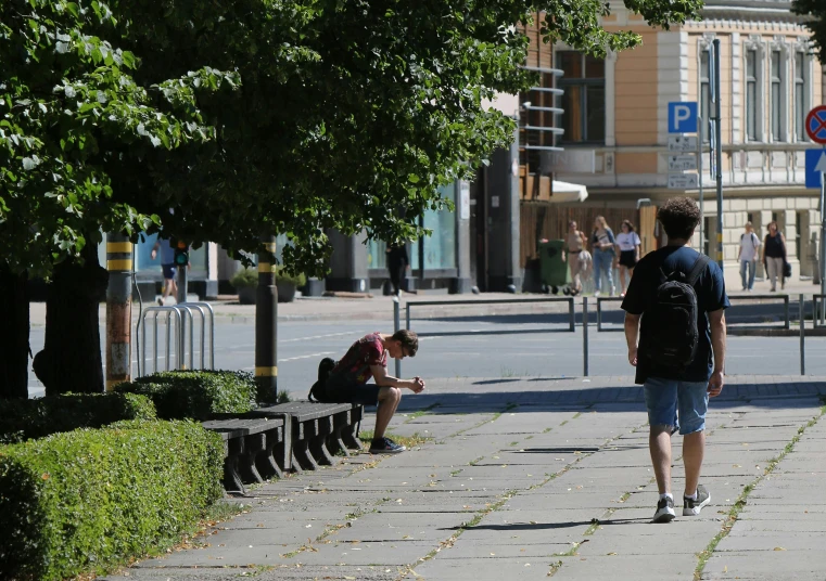 a person on a phone and another person sitting on a bench on a sidewalk