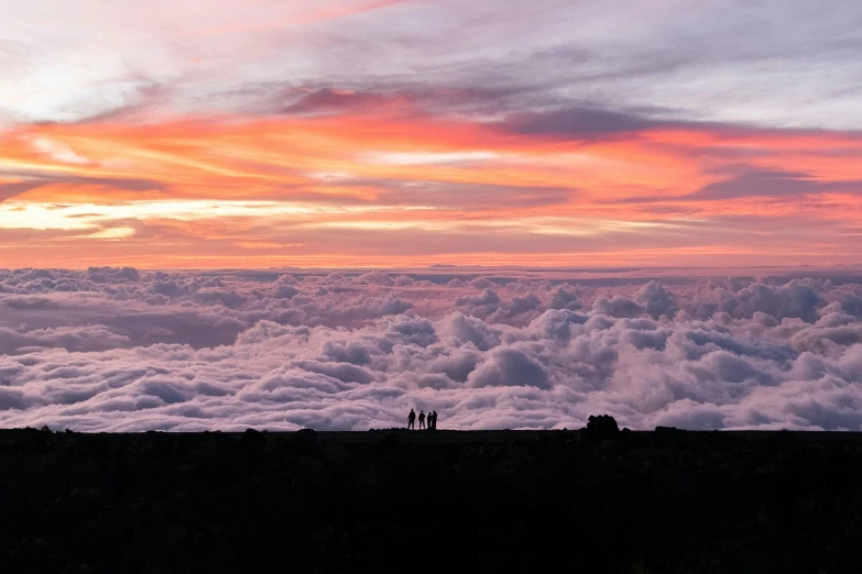 two people stand on the side of a mountain looking at clouds