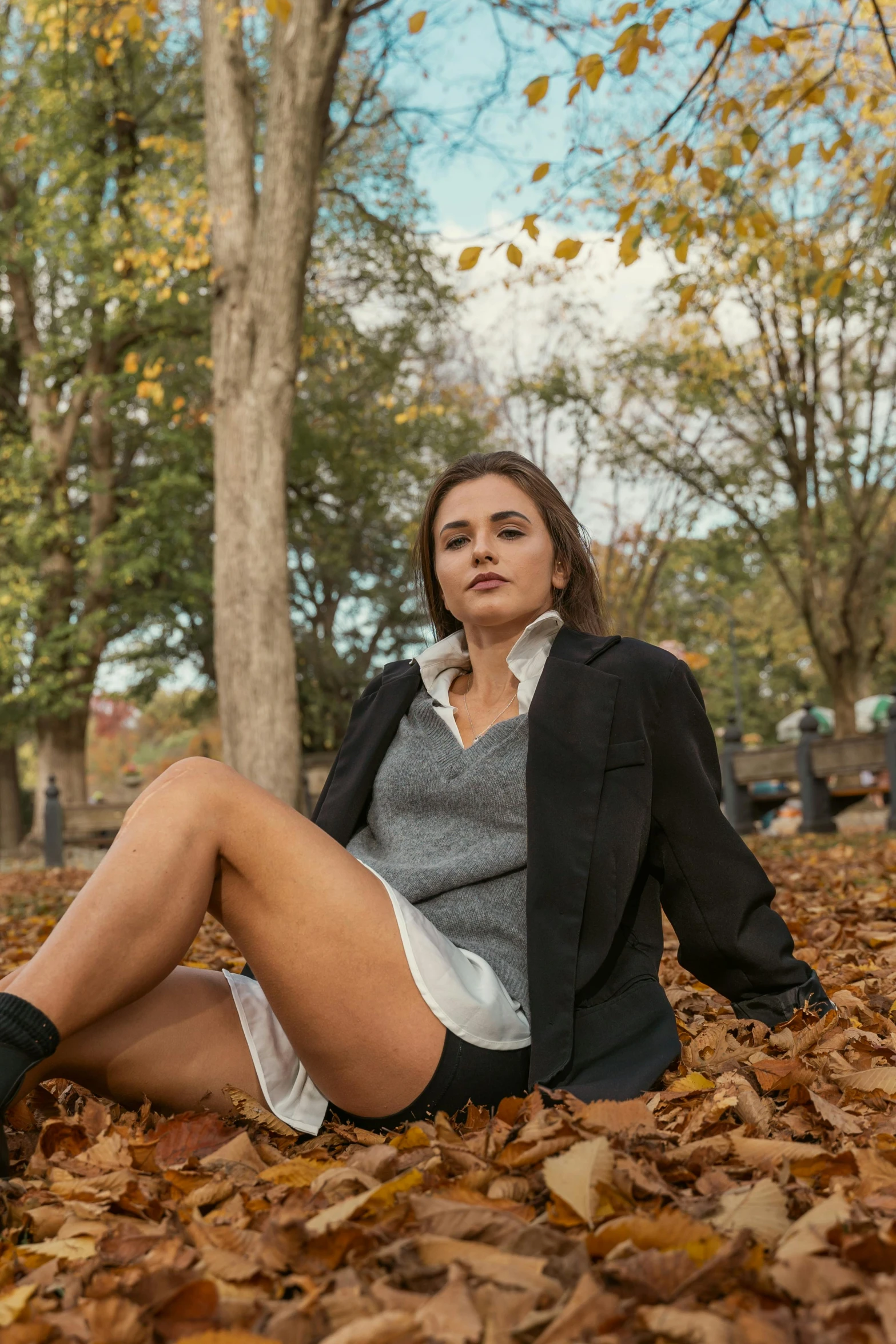 a woman is sitting on a pile of leaves in the fall