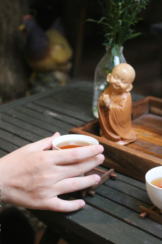 two cups of tea being held by people on a bench