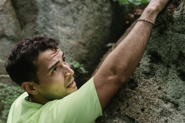 man in green shirt climbing on rocks with his hands under his head