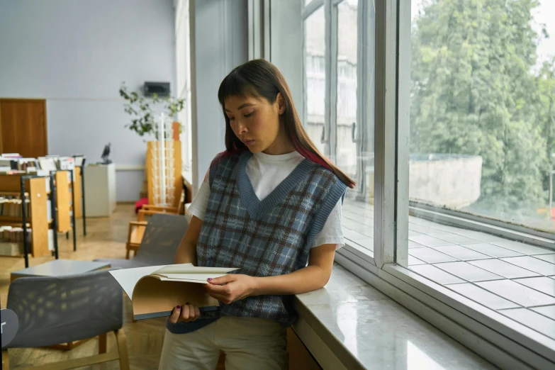 the girl is standing in front of the window holding papers