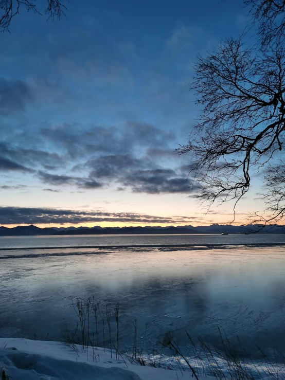 the sky is setting over the lake during the day