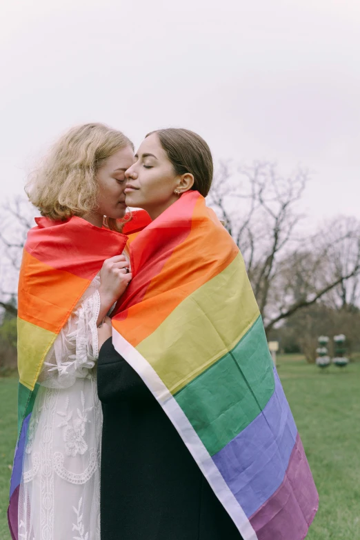 two women hugging each other and covering their faces with a colorful blanket