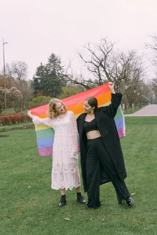 two woman holding a rainbow kite with their arms out