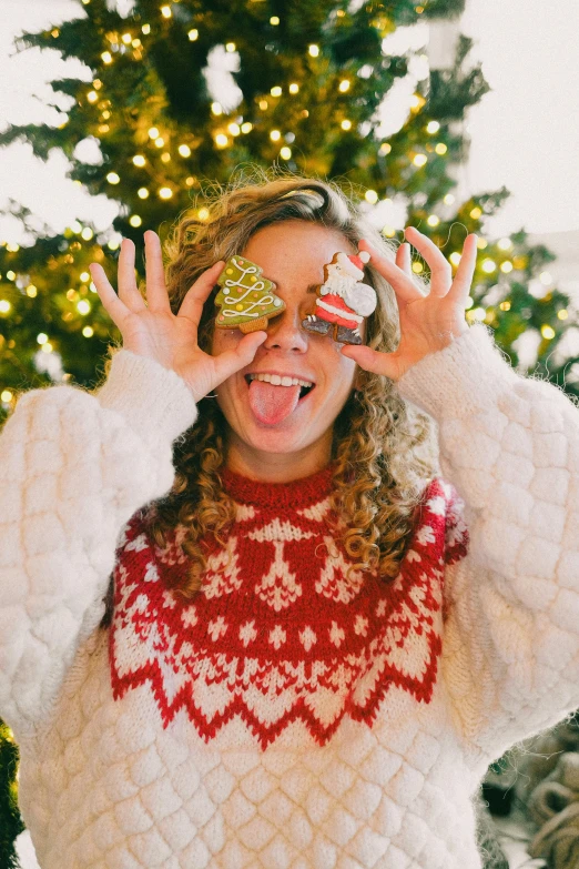 a woman making funny faces and holding candy bar in front of a christmas tree