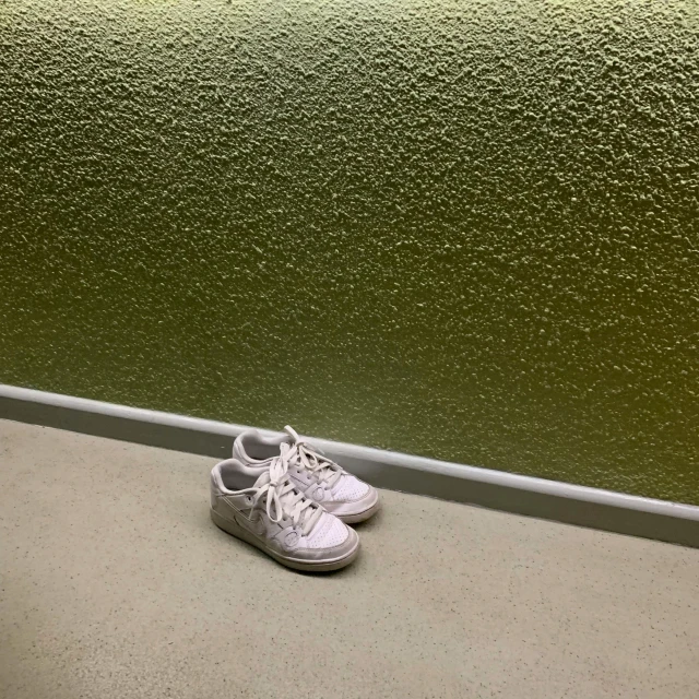 a pair of white tennis shoes sits next to a wall
