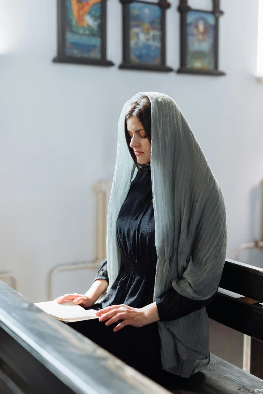 a woman wearing a gray shawl is sitting on the pews