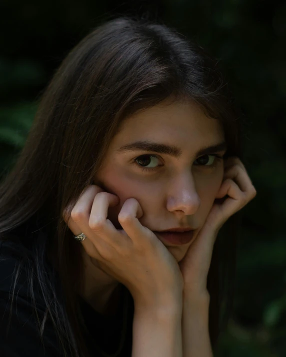 a woman sitting in front of a green bush