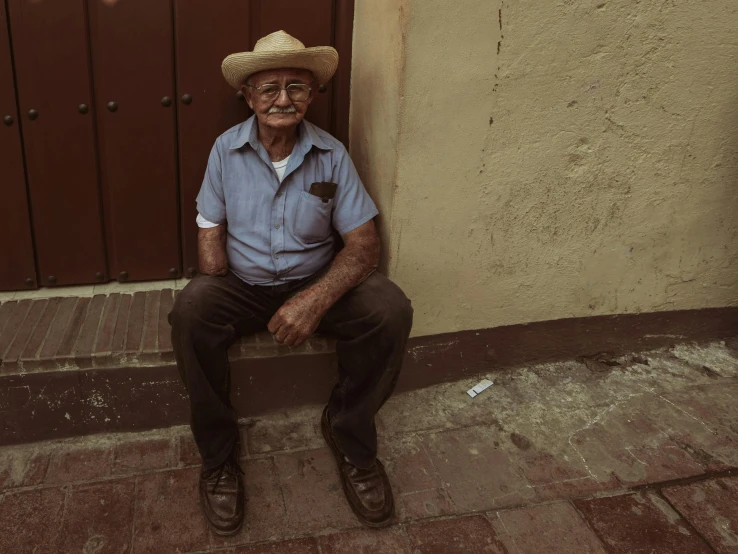 an older man wearing a hat and glasses sitting on steps