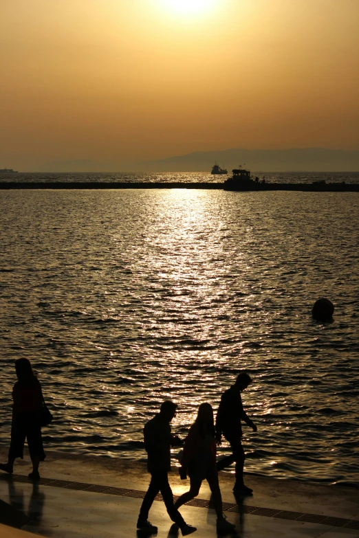 the people are walking on the beach in the evening