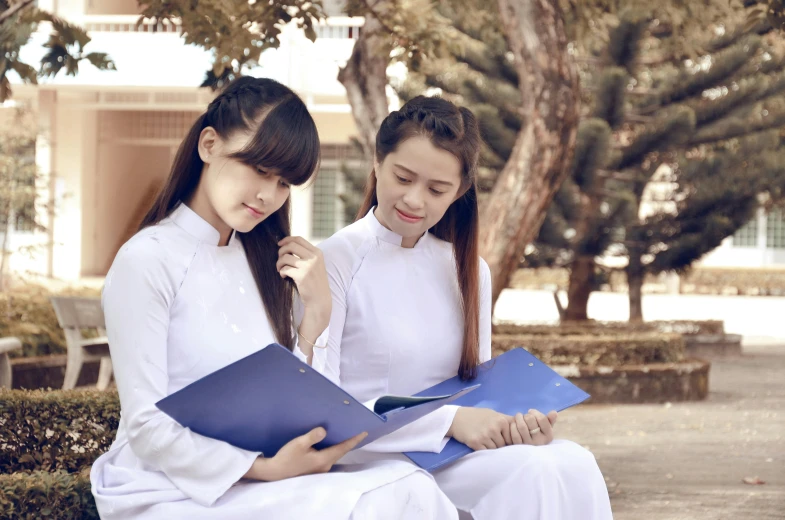 two girls in dress sit together reading books