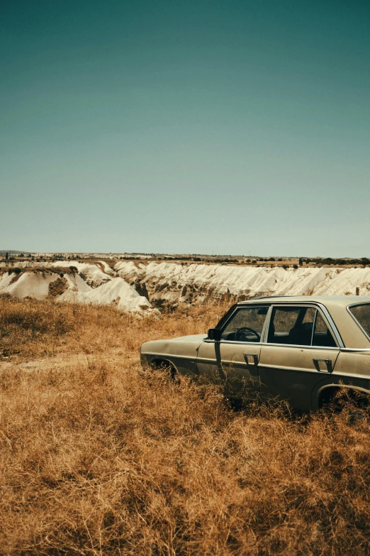 an abandoned car sits in a field of dried grass