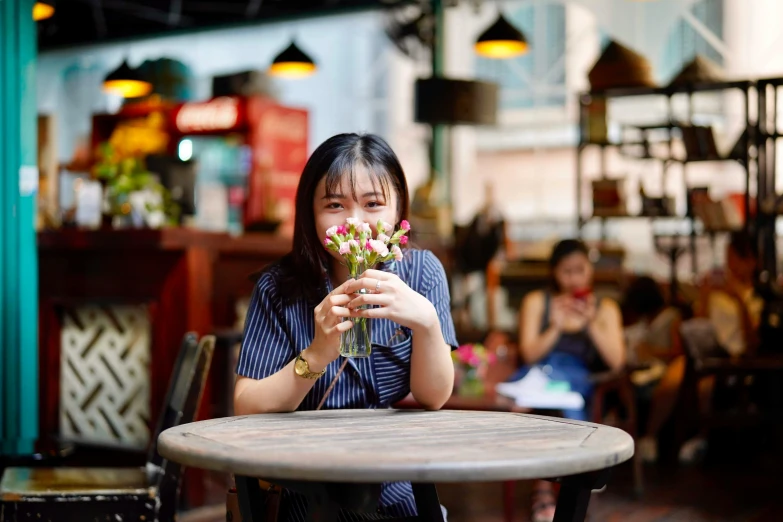 a woman sitting at a table with a flower in her hand