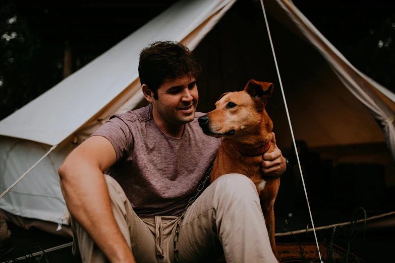 a young man squats next to a dog