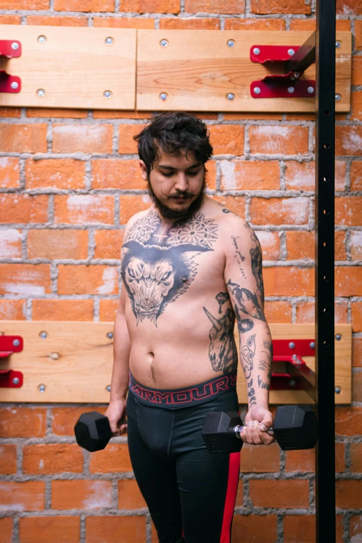 a tattooed man holds two black dumbs in his hands