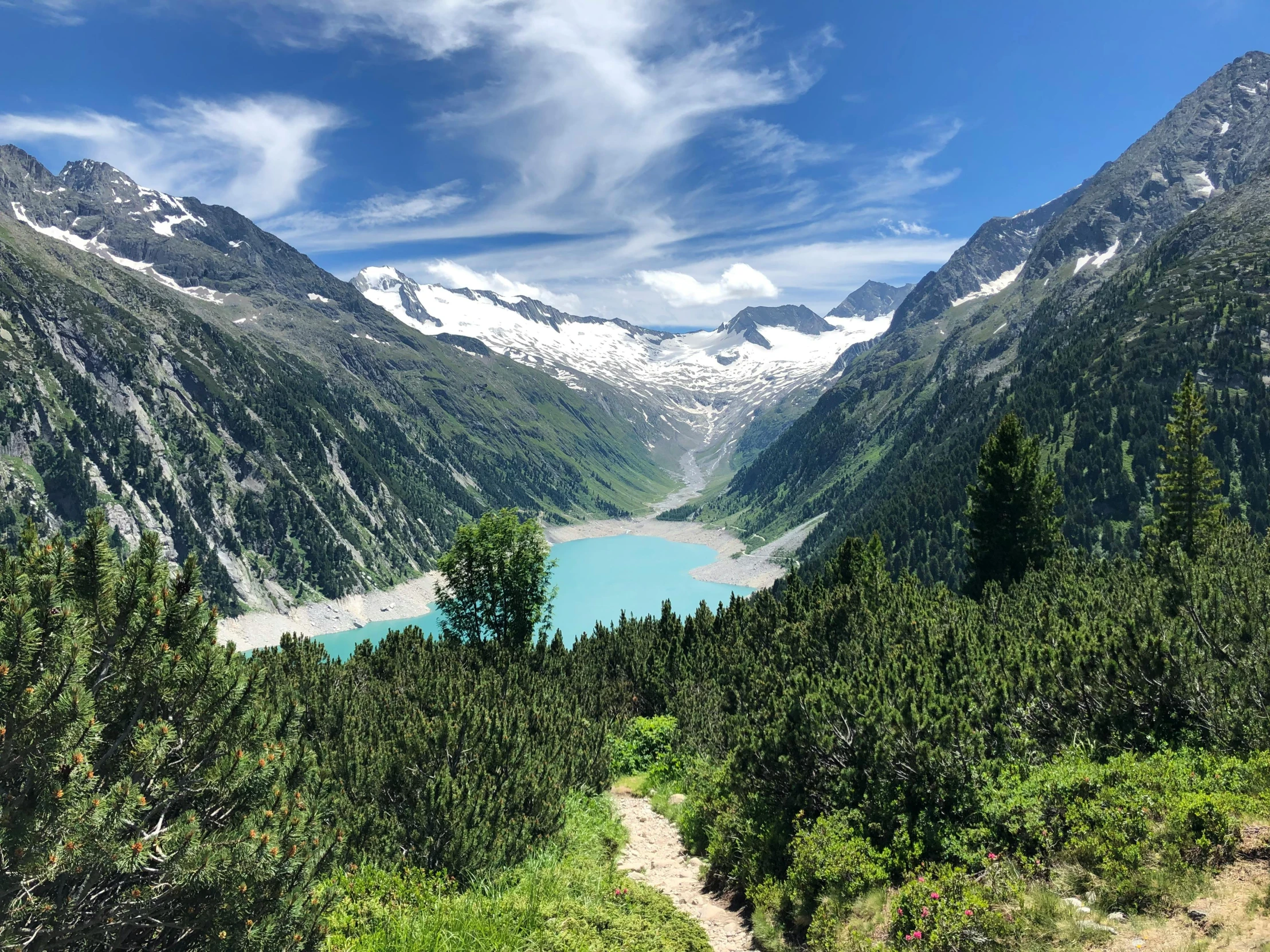 a path leading through a valley in the mountains with a lake