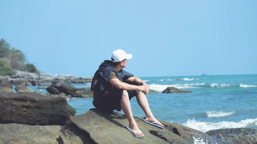 a man sits on a rock overlooking the ocean
