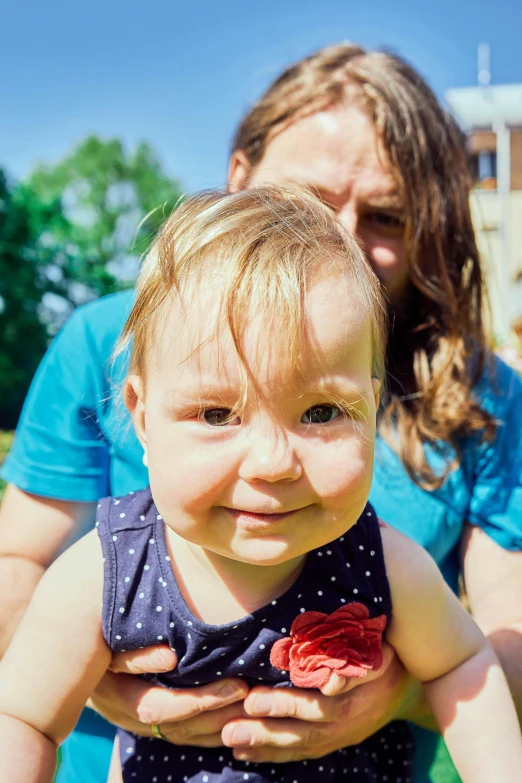 a little girl holding a flower in her lap while another woman holds her head