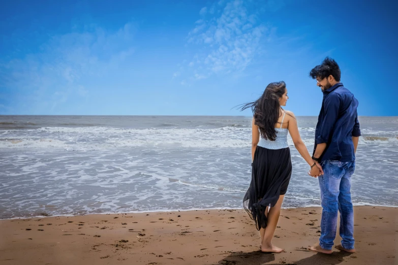 a man and woman standing on the shore looking at the waves