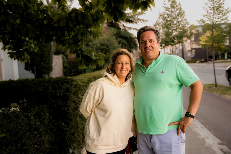 a man and woman smiling as they stand on the sidewalk