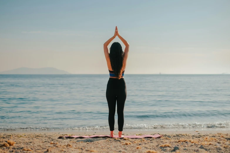 the back view of a woman doing yoga at the beach