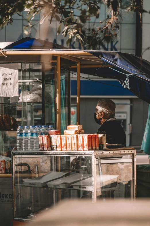 a man sitting outside in front of a drink stand