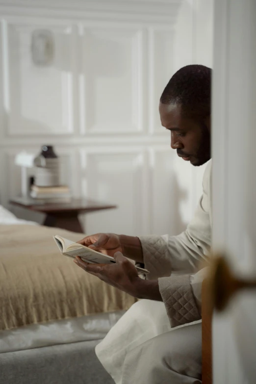 a man is sitting on a bed while reading a book