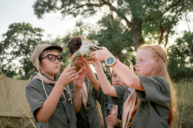 three children in uniform with their arm out to look at a turtle