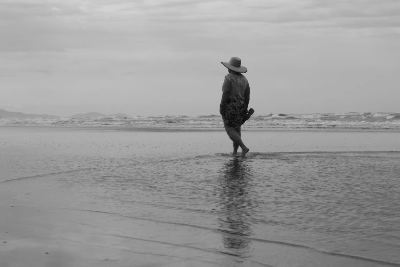 man in hat walking along the wet beach