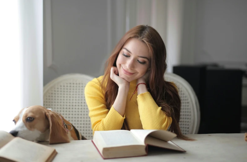 a young woman sitting at a table with her dog looking at an open book